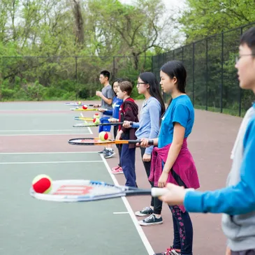 A line of children holding tennis rackets with tennis balls