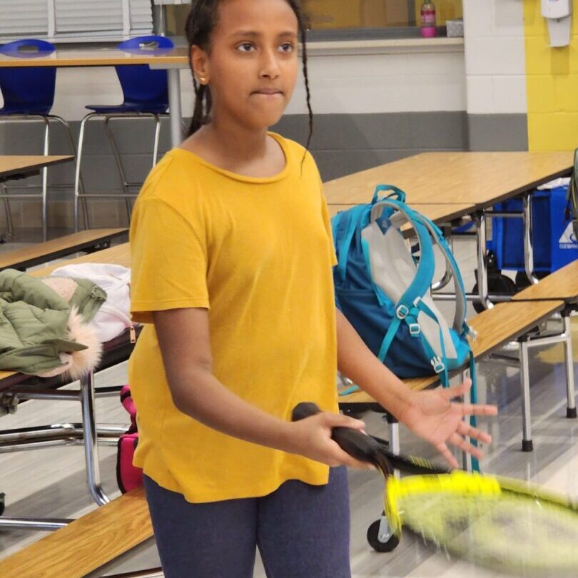 A young girl playing badminton indoors with a focused expression.